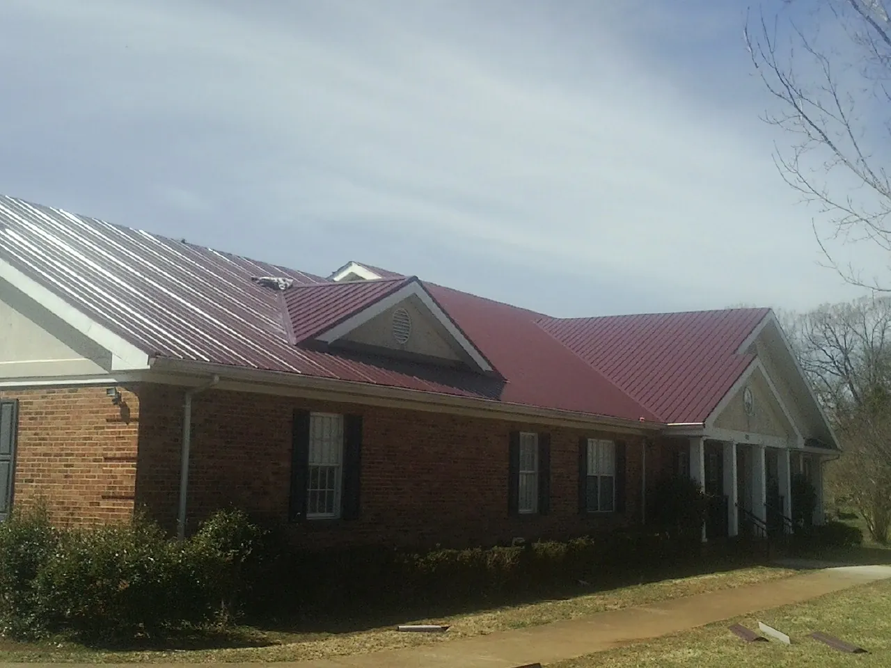 Red metal roof with gabled entries on a long brick building, from a Hail Damage Roof Repair job in Cloverdale