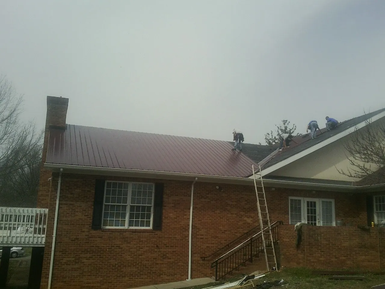 Crew setting red metal roofing panels on a brick home in Cloverdale