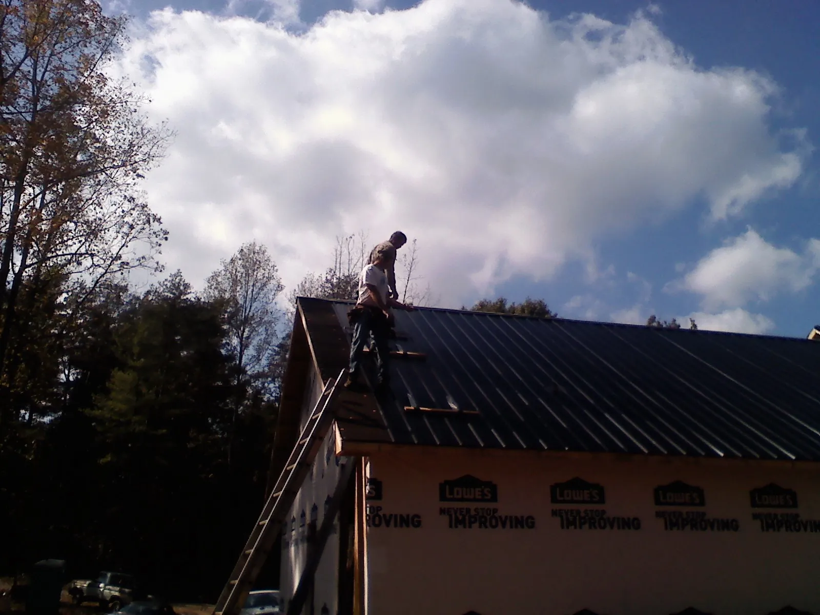 Roofer fastening dark metal panels high against a cloudy sky, from a Roof Inspection job in Cloverdale